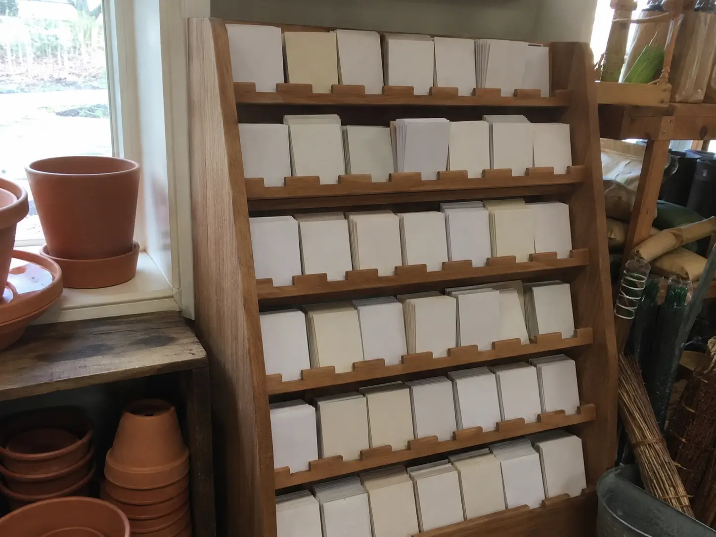A wooden seed display rack full of seed packets at a local garden center with terracotta pots nearby